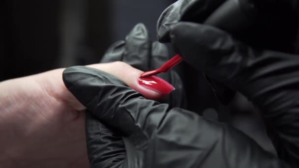 Femme ayant une manucure des ongles dans un salon de beauté avec une vue rapprochée d'un esthéticien appliquant un vernis avec un applicateur. Maître ongles peints avec vernis à ongles. Détails plan des mains appliquant ongle rouge . — Video