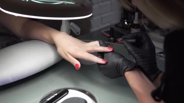 Kobieta o paznokci manicure w salon kosmetyczny i wyświetlić zbliżenie kosmetyczka stosowania lakieru z aplikatorem. Master pomalowane paznokcie z Polski paznokci. Szczegóły strzał rąk stosując czerwone paznokci. — Wideo stockowe