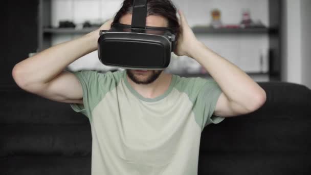 Молодий бородатий hipster людина почати використовувати його Vr гарнітура додатковий матч віртуальної реальності або перегляду 360 відео, сидячи на дивані в домашніх умовах, у вітальні. VR технологій. — стокове відео