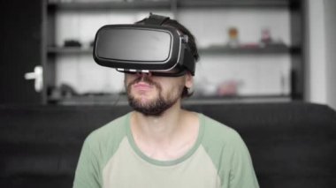 Genç kanepede oturan ve evde kurabiye oturma odasında yemek sırasında 360 video izlemek için onun Vr kulaklık görüntü kullanılarak hipster adam sakallı. VR teknolojisi.