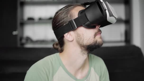 Ung skäggiga hipster man använder sin Vr headset display för virtuell verklighet spel eller titta på en 360-video och försökte röra till något han se medan du sitter på soffan. VR-tekniken. — Stockvideo