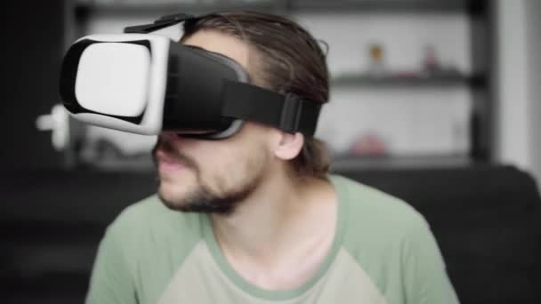 Młody Brodaty hipster człowieka za pomocą jego Vr zestaw słuchawkowy wyświetlacz dla wirtualnej rzeczywistości gry lub oglądania filmu 360 siedząc na kanapie w domu, w pokoju dziennym. Technologia VR. — Wideo stockowe