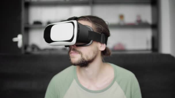 Молодий бородатий hipster людина за допомогою його Vr гарнітура дисплея для віртуальної реальності гри або перегляду 360 відео, сидячи на дивані в домашніх умовах, у вітальні. VR технологій. — стокове відео