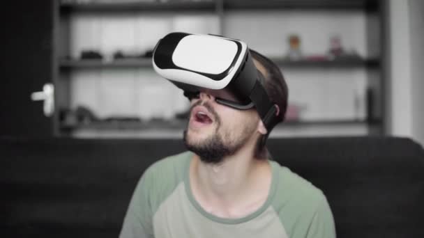 Homem jovem hipster barbudo usando sua exibição de fone de ouvido VR para o jogo de realidade virtual ou assistindo o vídeo 360 e tentando tocar em algo que ele vê enquanto está sentado no sofá. Tecnologia VR . — Vídeo de Stock