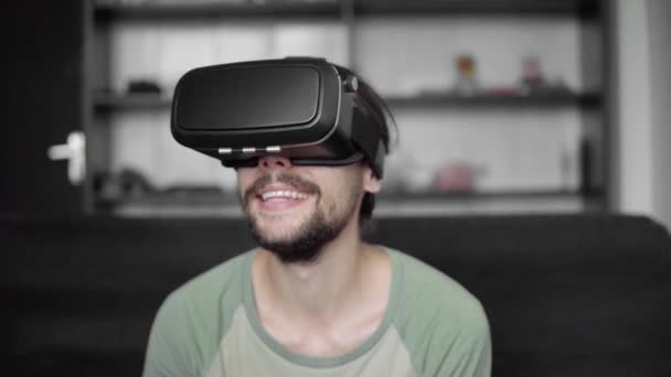 Щасливі молодих бородатий hipster людина за допомогою його Vr гарнітура дисплея для віртуальної реальності гри або перегляду 360 відео, сидячи на дивані в домашніх умовах, у вітальні. VR технологій. — стокове відео