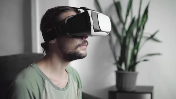 年轻胡子的时髦男子使用他的 Vr 耳机显示虚拟现实游戏或观看360视频, 并被一些东西吓坏了, 而坐在沙发上在家里的客厅. — 图库视频影像