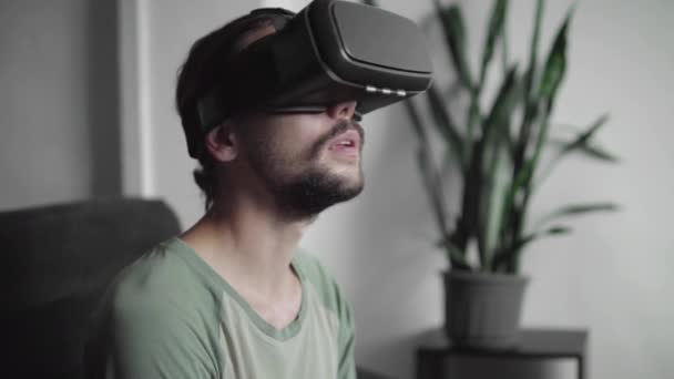 Ung skäggiga hipster man använder sin Vr headset display för virtuell verklighet spel eller titta på en 360-video och försökte röra till något han se medan du sitter på soffan. VR-tekniken. — Stockvideo