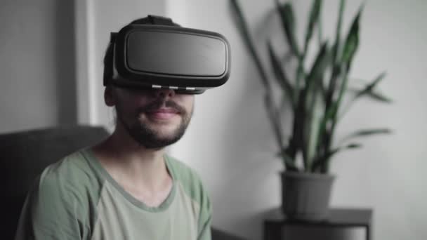 Joven hombre hipster barbudo utilizando su pantalla de auriculares VR para el juego de realidad virtual o ver el video 360 mientras está sentado en el sofá en casa en la sala de estar. Tecnología VR . — Vídeos de Stock