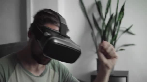 Joven hombre hipster barbudo utilizando su pantalla de auriculares VR para ver el video 360 y se siente como si estuviera en un concierto o discoteca mientras está sentado en el sofá en casa en la sala de estar. Tecnología VR . — Vídeo de stock