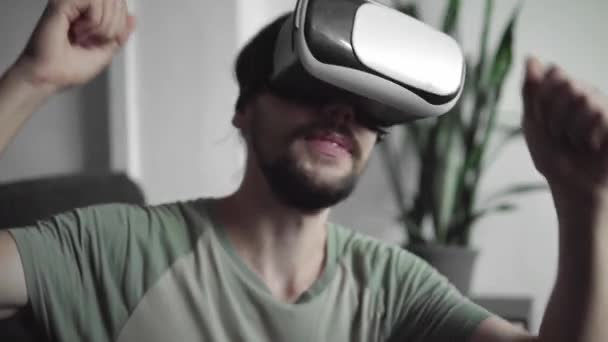 Pemuda berjenggot hipster pria menggunakan nya VR headset display untuk menonton 360 video dan merasa seperti dia berada di konser atau disko sambil duduk di sofa di rumah di ruang tamu. Teknologi VR . — Stok Video