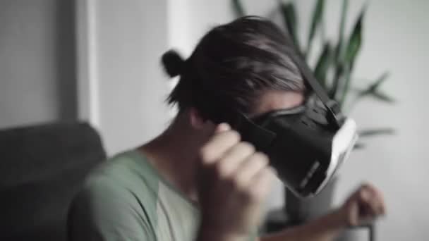 Joven hombre hipster barbudo utilizando su pantalla de auriculares VR para ver el video 360 y se siente como si estuviera en un concierto o discoteca mientras está sentado en el sofá en casa en la sala de estar. Tecnología VR . — Vídeo de stock