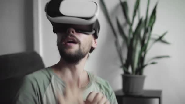 Young bebaarde hipster man zijn Vr headset weergave te gebruiken voor de virtuele werkelijkheid spel of kijken naar de 360 video en proberen te raken iets hij zien en vangen zittend op de Bank. Vr-technologie. — Stockvideo