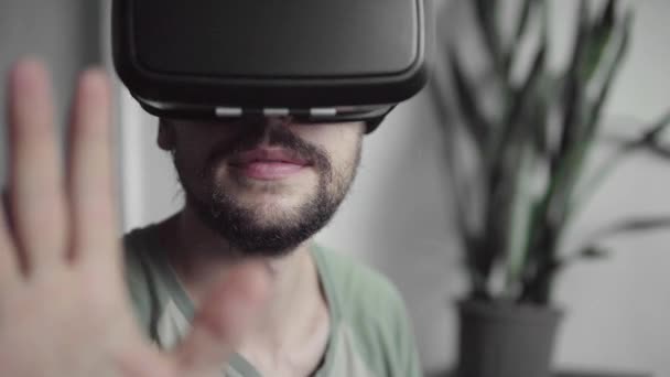 Młody Brodaty hipster człowieka za pomocą jego Vr zestaw słuchawkowy wyświetlacz dla wirtualnej rzeczywistości gry lub oglądania filmu 360 i starając się dotknąć aby coś widział, siedząc na kanapie. Technologia VR. — Wideo stockowe