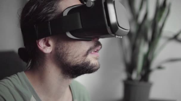 Молодий бородатий hipster людина за допомогою його відображення Vr гарнітура з навушниками віртуальної реальності матч або перегляду 360 відео, сидячи на дивані в домашніх умовах, у вітальні. VR технологій. — стокове відео