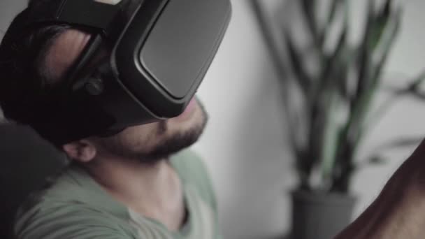 Joven hombre hipster barbudo usando su pantalla de auriculares VR con auriculares para el juego de realidad virtual o viendo el video 360 mientras está sentado en el sofá en casa en la sala de estar. Tecnología VR . — Vídeo de stock