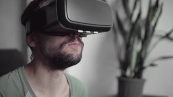 Молодий бородатий hipster людина за допомогою його відображення Vr гарнітура для перегляду 360 відео під час сидить на дивані і їсть печиво вдома у вітальні. VR технологій. — стокове відео