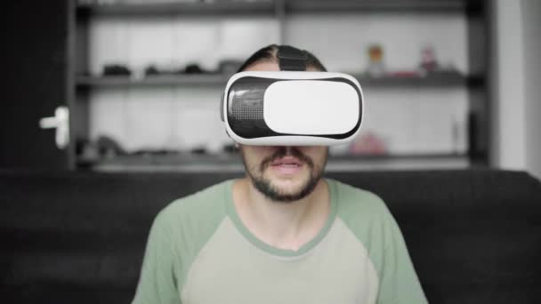 Молодой бородатый хипстер использует свой VR гарнитуру дисплей для игры в виртуальную реальность или смотреть 360 видео, сидя на диване в гостиной. Технологии . — стоковое видео