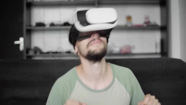 Молодой бородатый хипстер, используя свой VR гарнитуру дисплей для просмотра 360 видео и чувствует, как он находится на концерте или диско, сидя на диване в гостиной. Технологии . — стоковое видео