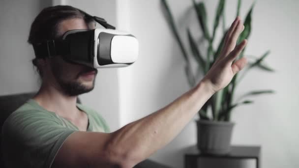 Młody Brodaty hipster człowieka za pomocą jego Vr zestaw słuchawkowy wyświetlacz dla wirtualnej rzeczywistości gry lub oglądania filmu 360 i starając się dotknąć aby coś widział, siedząc na kanapie. Technologia VR. — Wideo stockowe