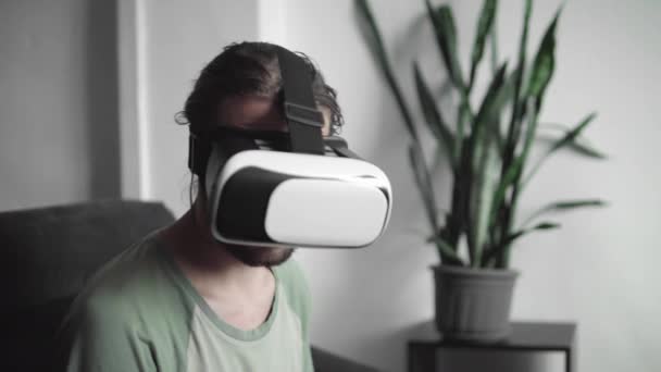Junger bärtiger Hipster-Mann, der sein vr-Headset-Display für Virtual-Reality-Spiele benutzt oder sich das 360-Video ansieht, während er zu Hause auf dem Sofa im Wohnzimmer sitzt. vr-Technologie. — Stockvideo