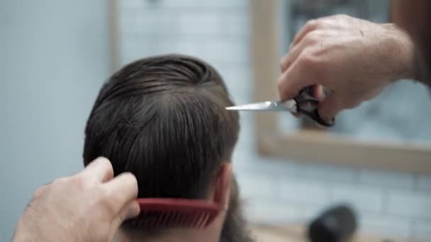 Close-up de barbeiro corta o cabelo por tesoura na barbearia. Cabeleireiros mãos no processo de trabalho. Barbeiro fazendo corte de cabelo de homem barbudo atraente na barbearia. Cabeleireiro no trabalho. Salão de beleza . — Vídeo de Stock