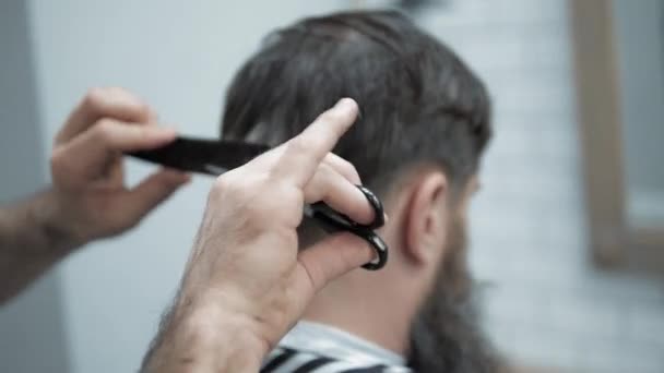 Close-up de barbeiro corta o cabelo por tesoura na barbearia. Cabeleireiros mãos no processo de trabalho. Barbeiro fazendo corte de cabelo de homem barbudo atraente na barbearia. Cabeleireiro no trabalho. Salão de beleza . — Vídeo de Stock