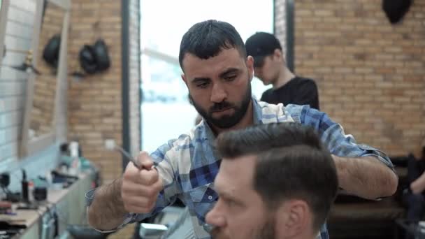 Close-up de barbeiro corta o cabelo por tesoura na barbearia. Cabeleireiros mãos no processo de trabalho. Barbeiro fazendo corte de cabelo de homem barbudo atraente na barbearia. Cabeleireiro no trabalho. Salão de beleza . — Vídeo de Stock