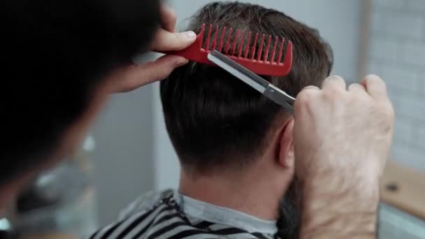 El primer plano del peluquero corta el cabello con tijeras en la barbería. Peluqueros manos en el proceso de trabajo. Peluquero haciendo corte de pelo de hombre barbudo atractivo en la barbería. Peluquería en el trabajo. Salón de belleza . — Vídeos de Stock