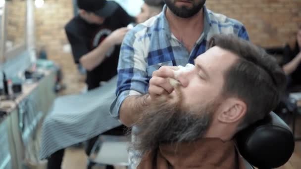 Friseur rasiert Männer mit langem Bart mit Rasierklinge im Friseursalon oder Friseursalon. Herrenfrisur und Rasur beim Friseur, Friseur und Rasiersalon. — Stockvideo