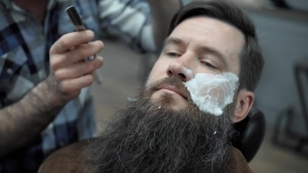 Peluquero afeita a los hombres con una barba larga con hoja de afeitar recta en s peluquería o barbería. Mans corte de pelo y afeitado en la peluquería, peluquería y salón de afeitar . — Vídeos de Stock