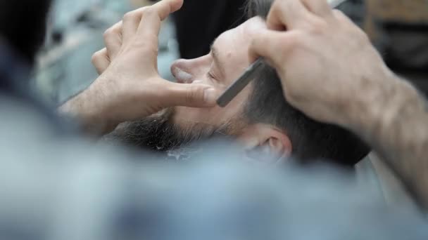 Kapper scheert mannen met een lange baard met rechte scheermesje in s kapsalon of barbershop. Mans kapsel en scheren bij de kapper, Kapper en scheren salon. — Stockvideo