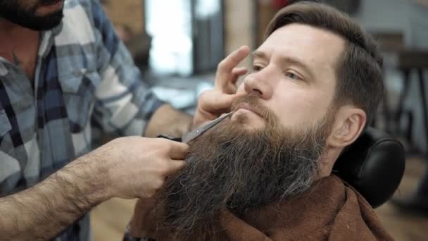 Barbier faire barbe coupe de cheveux avec des hommes adultes avec une longue barbe dans le salon de coiffure des hommes. Le toilettage de la barbe. Salons de coiffure sur le lieu de travail. Coiffure et coupe de barbe dans un salon de coiffure . — Video