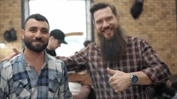 O Barbeiro e o seu cliente feliz na barbearia. A arrumar a barba. Cabeleireiros no local de trabalho. Penteado de barba e corte de cabelo em uma barbearia . — Vídeo de Stock