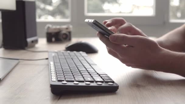 Mladý muž používající mobilní telefon smartphone v sedle počítačovou klávesnici a myš. Na volné noze pracuje a používání telefonu pro komunikaci s klienty. — Stock video