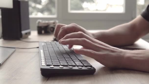 Junger Mann tippt auf einer Tastatur und bedient sich dann eines Tablets. Freiberuflicher Fotograf, der mit Tablets arbeitet und mit Kunden kommuniziert. — Stockvideo