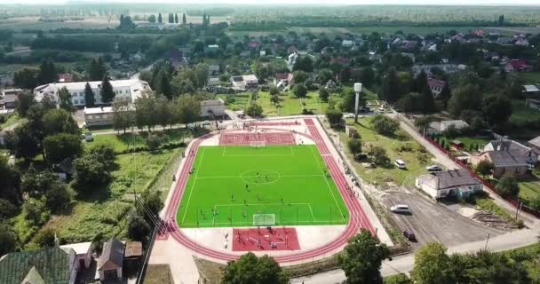 Boş spor bahçesi kuş bakışı görünüme köyden stadyumda. Kırmızı spor büyük tenis ve basketbol oynamak için zemin. Futbol futbol sahası yeşil ve yollar çalıştıran. — Stok video