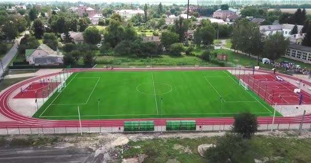 Estádio de playground esporte vazio na aldeia a partir de aves vista para os olhos. Vermelho campo de esporte para jogar tênis grande e basquete. Campo de futebol verde e estradas em execução . — Vídeo de Stock