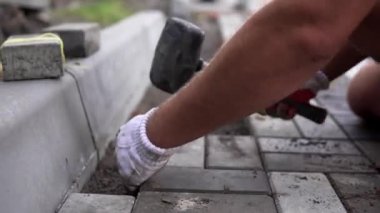 Onun turuncu bir üreticisi eller eller dikkatle yerleştirerek bir pozisyonda düzeltilmiş ve komisyonlu topraklarında temel yeni dış parke taşı döşeme uydurma bir çekiçle eldivenli. Kum Vakfı. Bina.