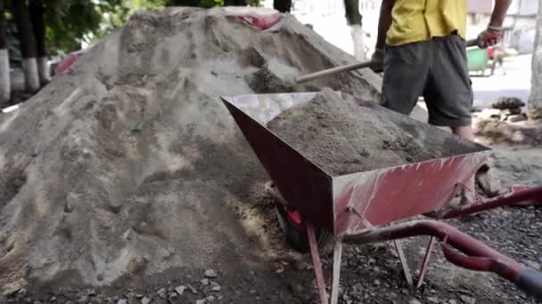 Trabajador utilizar la pala y llenar la carretilla con arena para la construcción de la carretera de la acera. Herramientas de construcción. Pala y el carro sobre ruedas con arena en la construcción de las carreteras . — Vídeo de stock