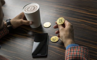 Zengin bir bitcoin para tutan ve bir masaya bitcoin telefon ve altın sikkeleri ile bir kahve içme dostum. Bitcoins incelemesi üzerinden kar.