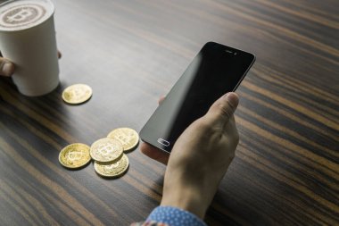 Zengin bir bitcoin para tutan ve bir masaya bitcoin telefon ve altın sikkeleri ile bir kahve içme dostum. Bitcoins incelemesi üzerinden kar.