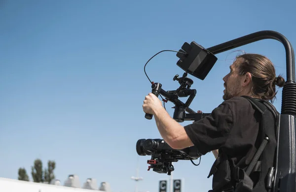 Professionele videograaf vasthouden van de camera op 3-axis gimbal die gemonteerd op gemakkelijk tuig. Videograaf gebruiken steadicam. Pro apparatuur helpt om hoge kwaliteit video zonder schudden. — Stockfoto