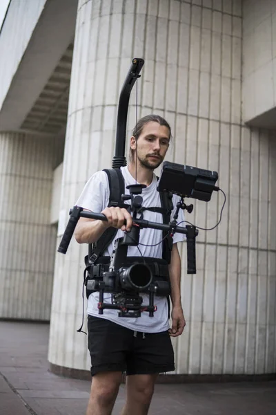 Professional videographer holding camera on 3-axis gimbal which mounted on easy rig. Videographer using steadicam. Pro equipment helps to make high quality video without shaking. — Stock Photo, Image