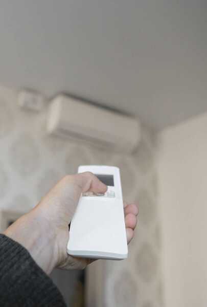 Hand with remote control directed on the conditioner on the wall. Mans hand using remote control open The air conditioner is cooled to 25 degrees Celsius in his bedroom.
