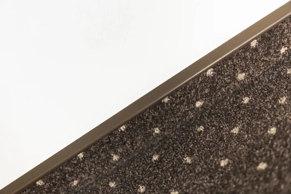 Suelo de alfombra marrón con puntos blancos con un zócalo de alfombra en una pared blanca . — Foto de Stock