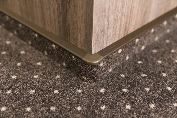 Brown carpet floor with a white dots with a carpet baseboard on a wood-based panels wall.