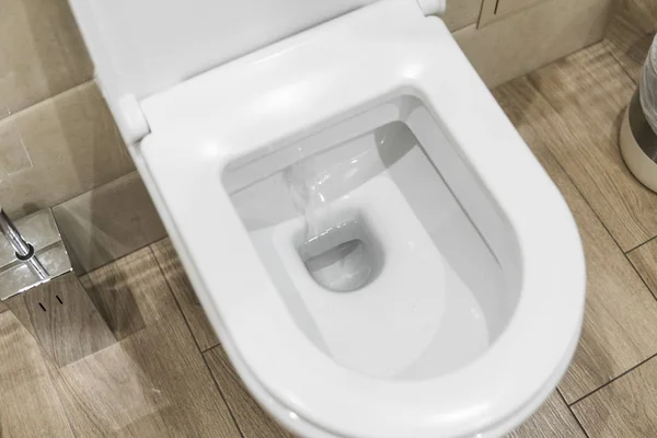 Bol de toilette blanc dans une salle de bain. Vue rapprochée d'une toilette blanche à chasse d'eau. L'eau tourbillonne dans la cuvette . — Photo