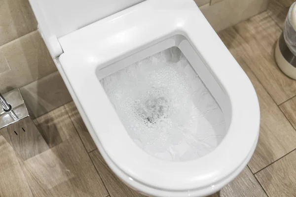 White toilet bowl in a bathroom. Closeup view of a flushing white toilet. The water swirls in the toilet bowl. — Stock Photo, Image