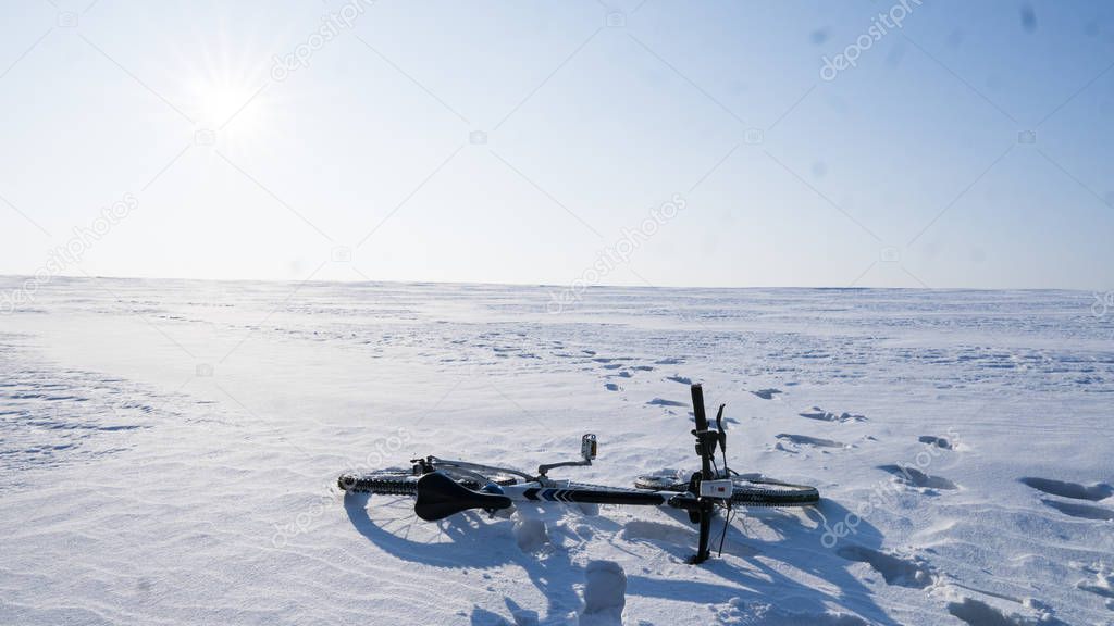 Mountain bike lying on a white snow on a winter field with a blue sky on background.