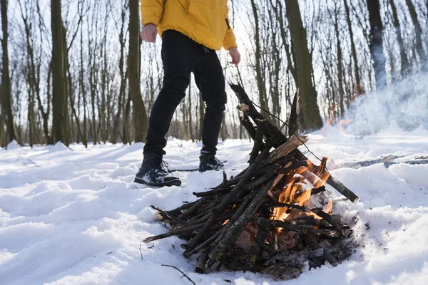 Kış Orman ayakta yakınındaki küçük bir yangın sarı ceketli genç adam.